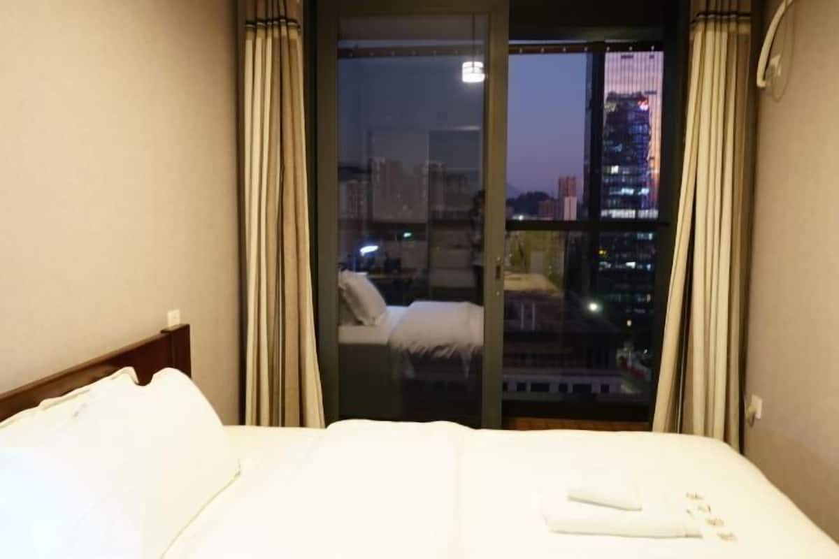 Habitación de hotel con cama, puerta corrediza al balcón y vistas panorámicas de la ciudad.