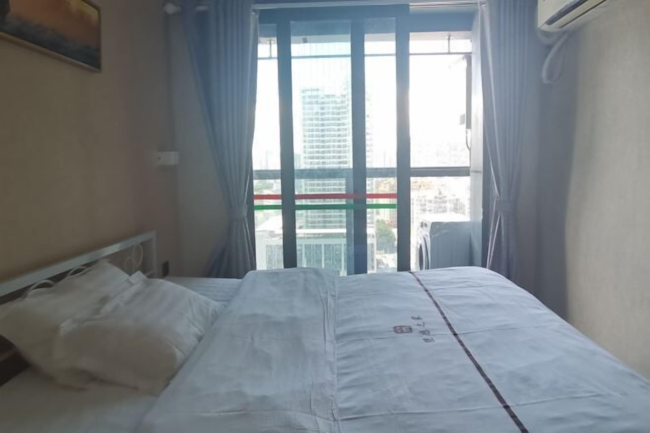 A hotel room with a bed, a window with curtains, and an air conditioning unit.