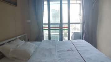 A hotel room with a bed, a window with curtains, and an air conditioning unit.