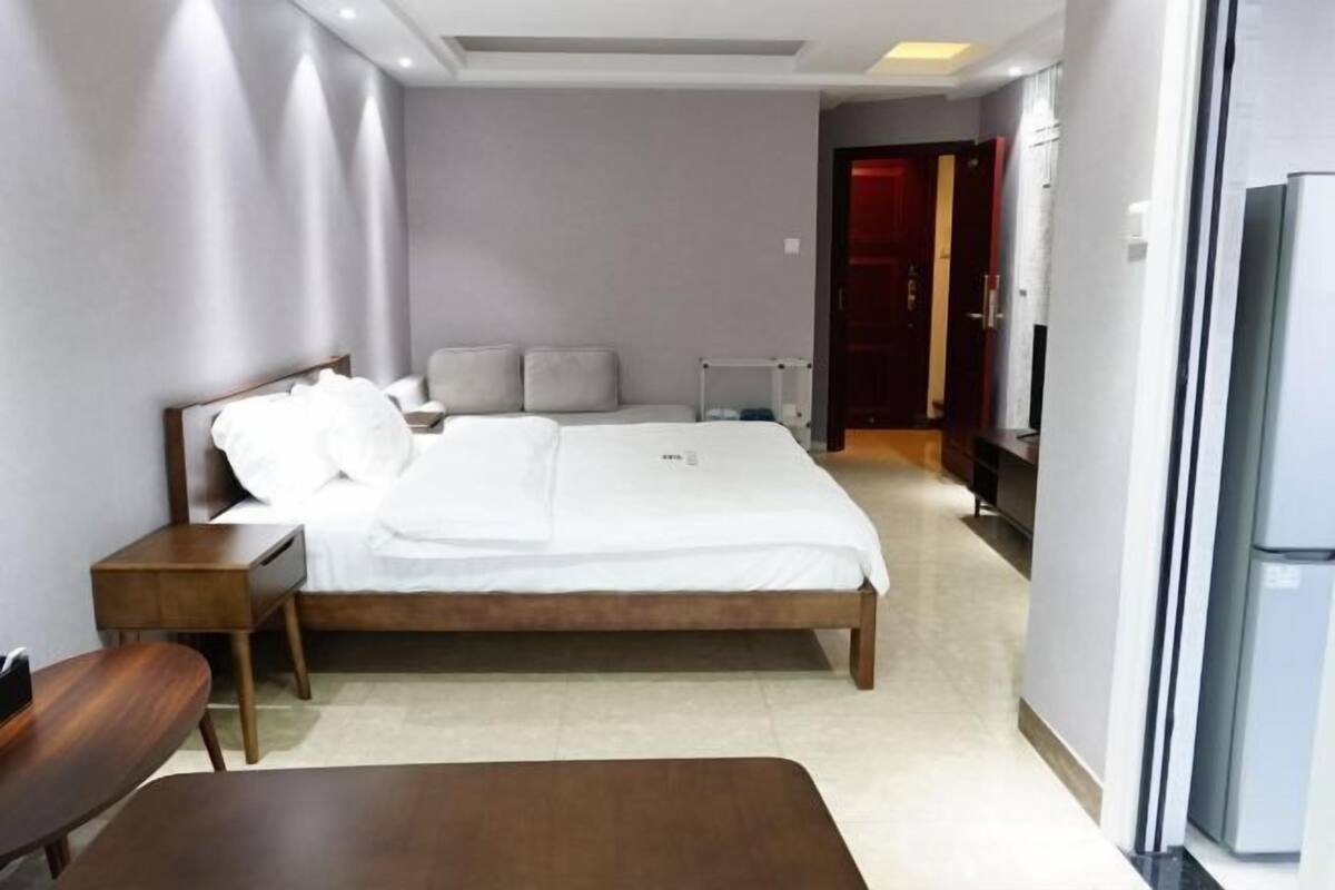 Una habitación de hotel moderna con una cama de madera, una mesita de noche, una silla y un escritorio.