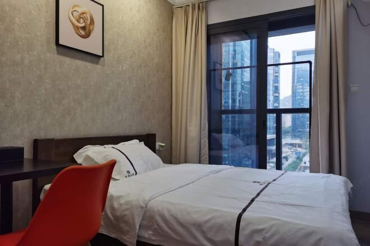 Habitación de hotel con cama, una silla, ventana con vista a la ciudad y un cuadro en la pared.
