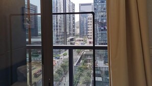 Une vue à travers une fenêtre dont le cadre est en métal, donnant sur des immeubles modernes et des routes bordées de verdure.