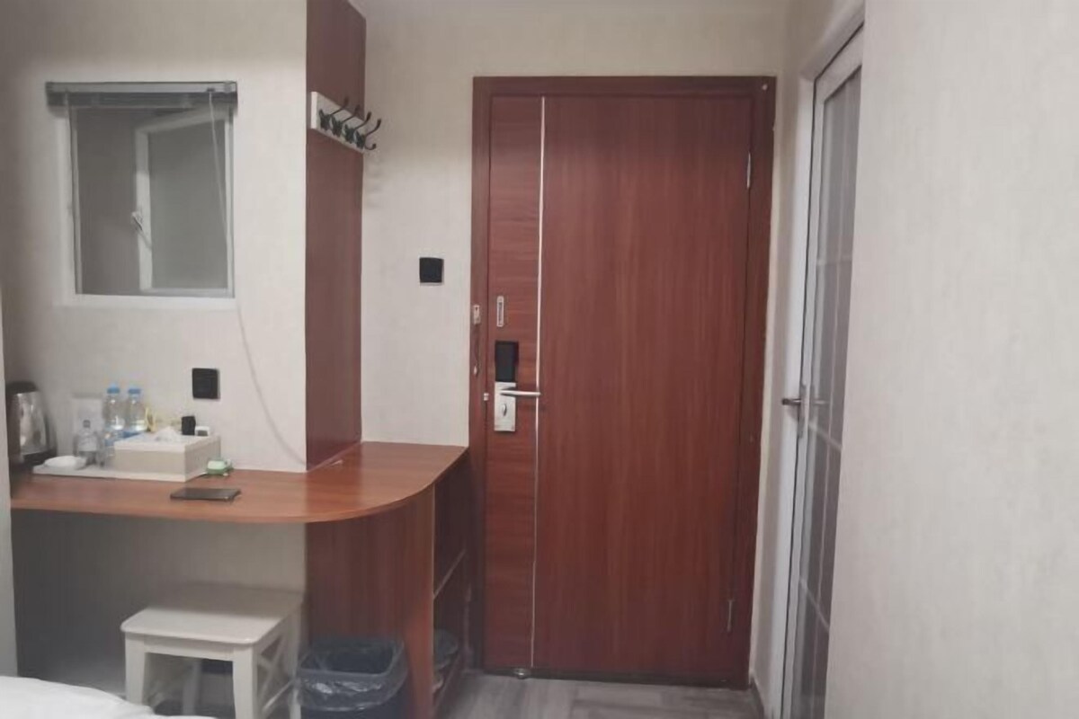 Une chambre d’hôtel compacte, dotée d’un bureau en bois, d’une petite table blanche, d’une poubelle et d’une armoire avec un miroir.