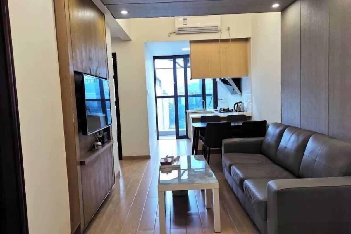 Una sala de estar moderna con un sofá de cuero, una mesita de centro pequeña y un televisor de pantalla plana montado sobre un mueble de madera.