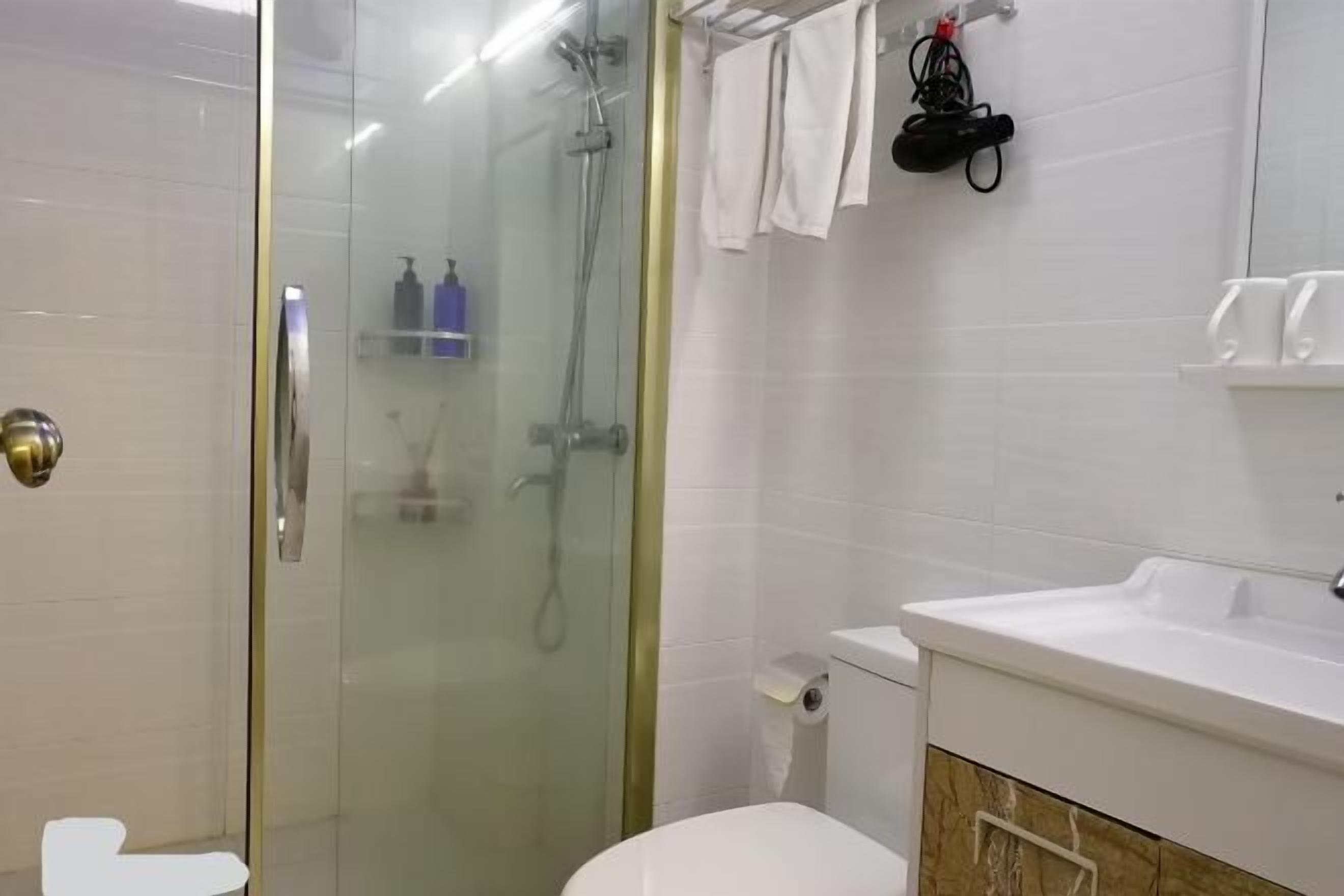 A modern bathroom with a glass-enclosed shower, a white toilet, and a sink with a marble countertop.