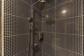 Une salle de bain dotée d’un espace douche avec un mur recouvert de carreaux disposés en motif quadrillé et d’un pommeau de douche à main.