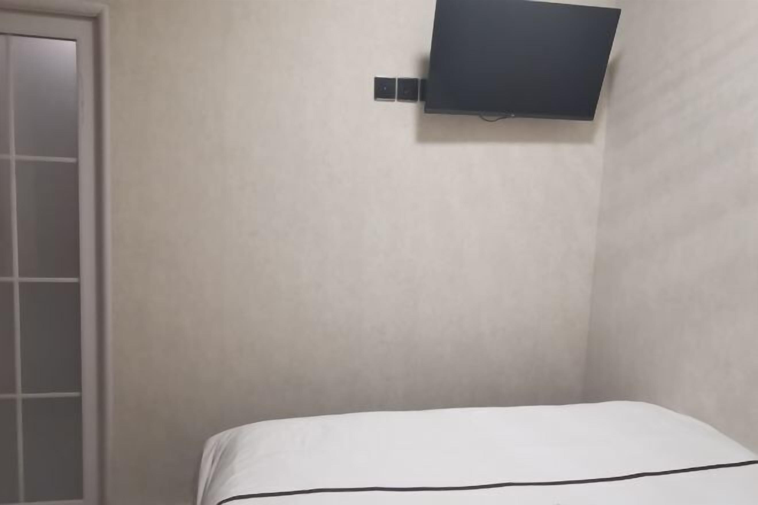 Une pièce avec un lit, un téléviseur fixé au mur et une porte.