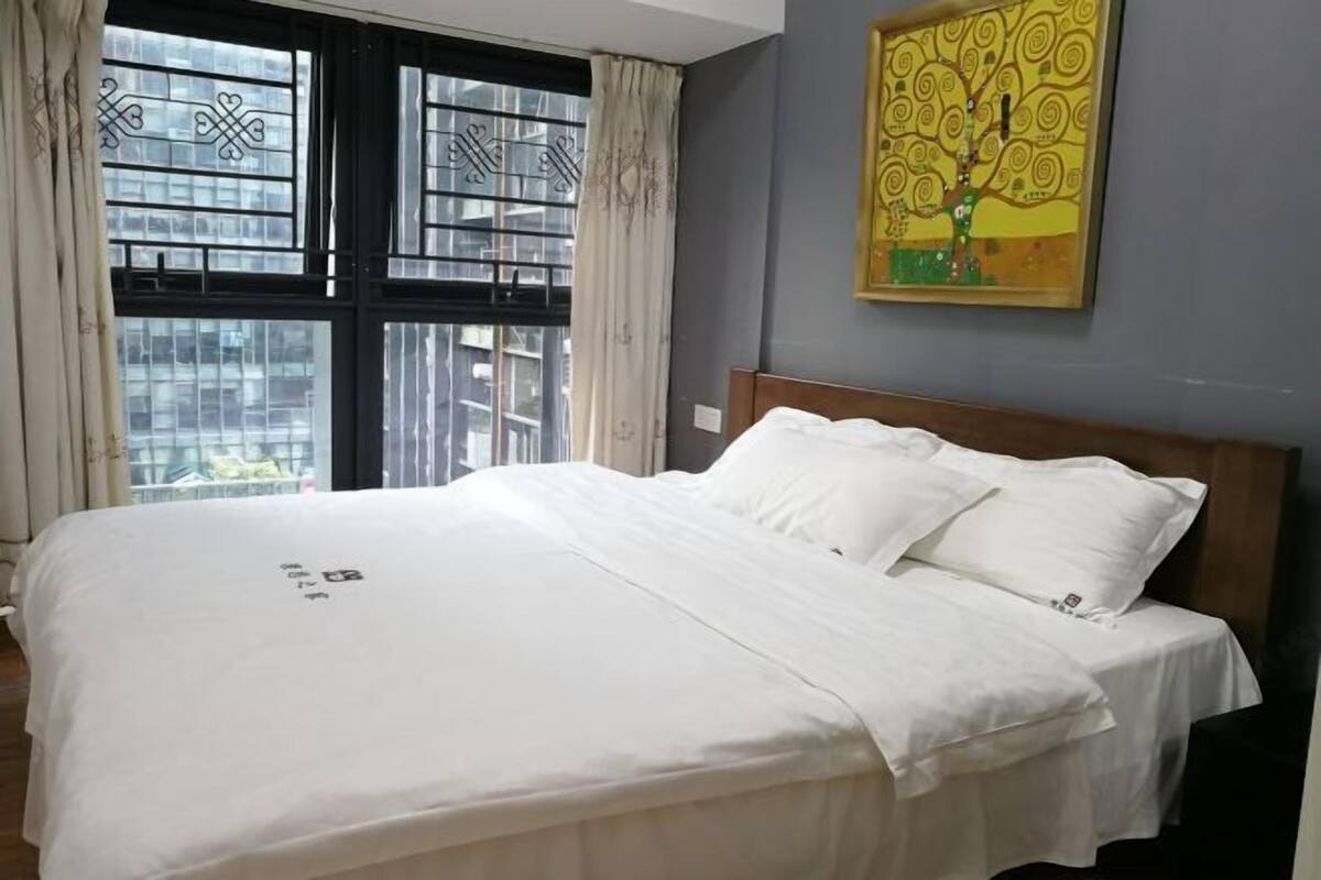 Una cama bien hecha con sábanas blancas en una habitación con un ventanal grande y un cuadro en la pared.