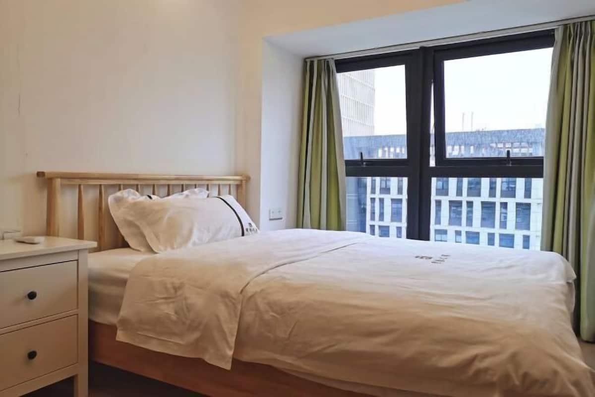 Una cama bien hecha con sábanas blancas, cabecera de madera y una mesita de noche con cajones.