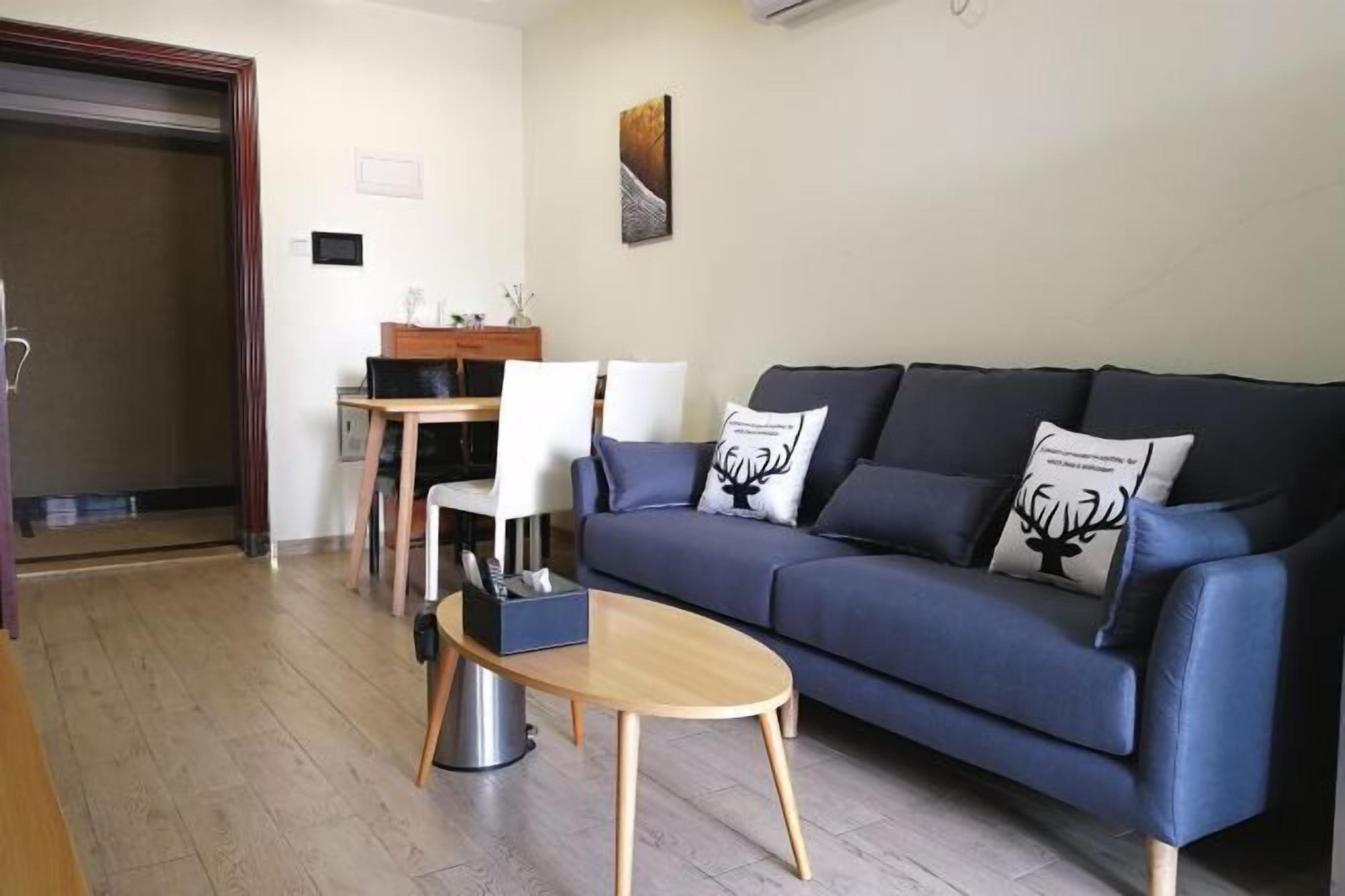 A living room with a dark blue sofa, a wooden coffee table, and a dining area with a wooden table and chairs.