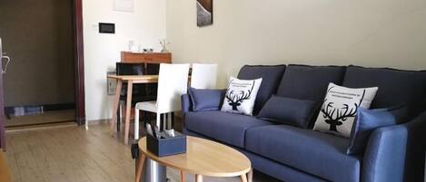 Una sala de estar con un sofá azul oscuro, una mesa de centro de madera y un comedor con una mesa y sillas de madera.