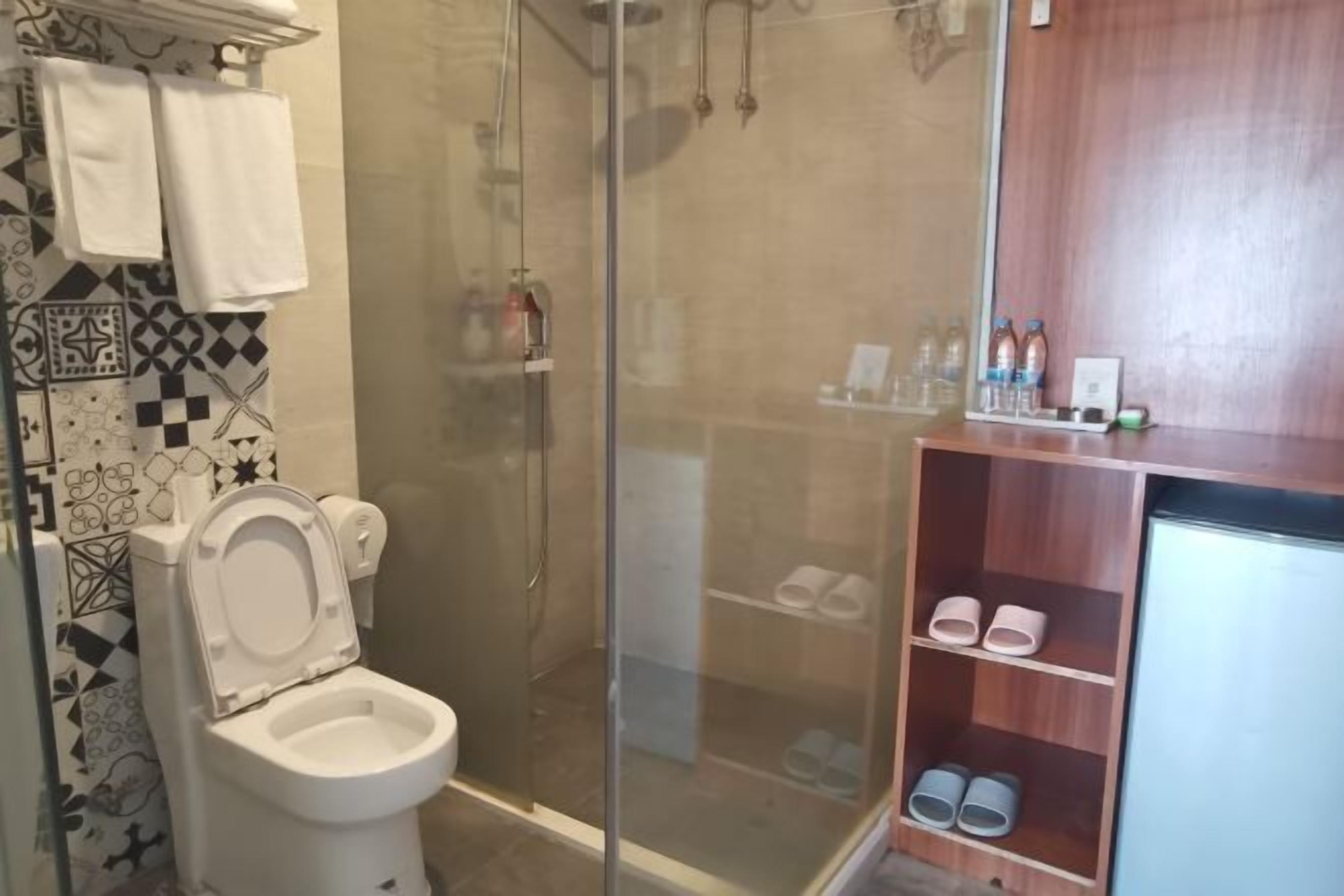 Un baño con inodoro, ducha y estante con pantuflas.