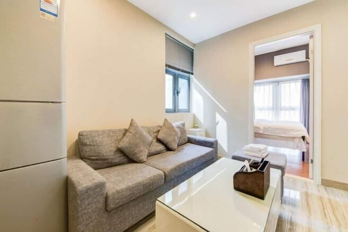 Una sala moderna con un sofá gris, una mesita de centro de vidrio y una pequeña mesa auxiliar.