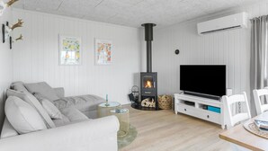 En moderne stue med en hvid sofa, et fladskærms-tv, en sort brændeovn og et spiseområde med et bord og stole.