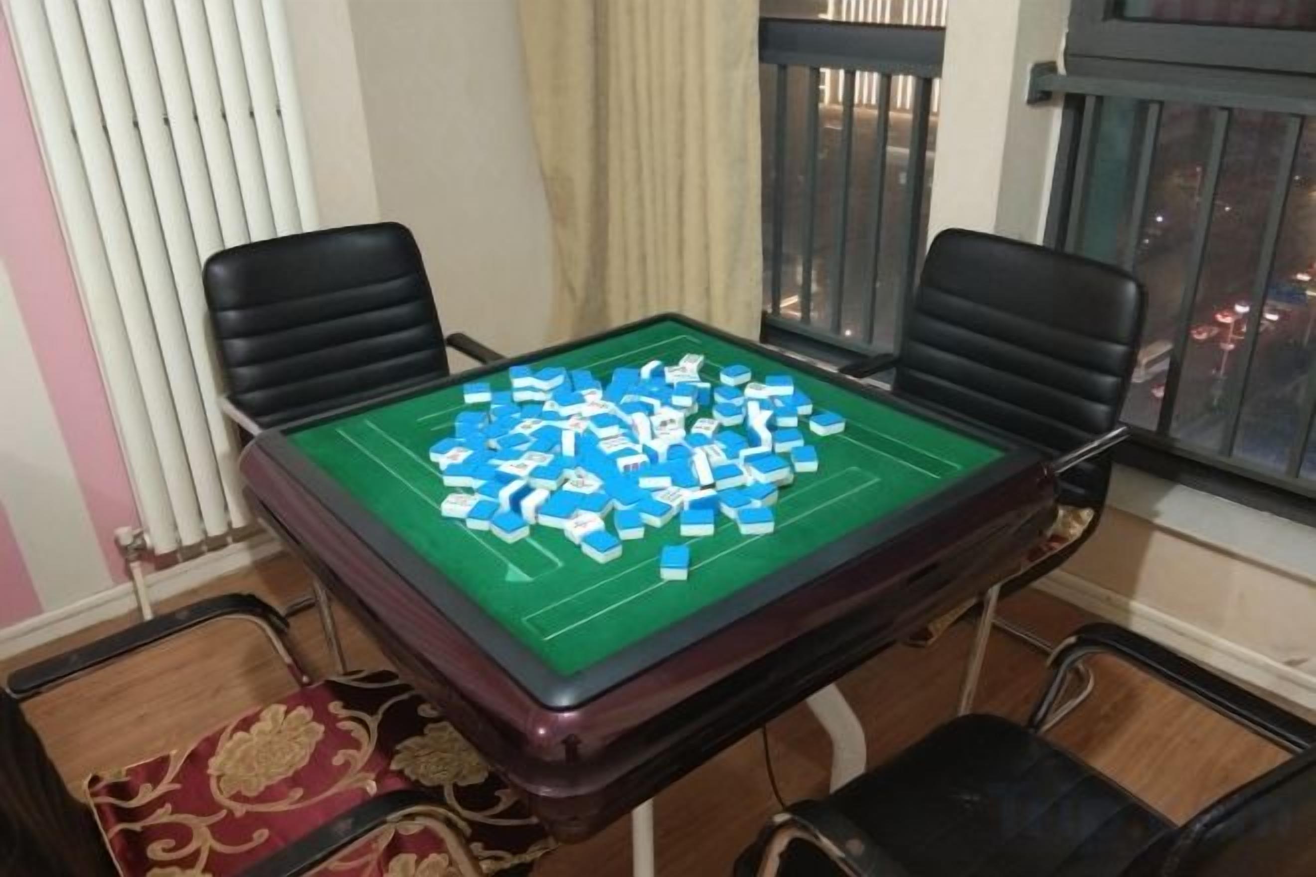 Une pièce avec une table verte pour jouer à des jeux de société, quatre chaises, une fenêtre avec des stores et un radiateur.