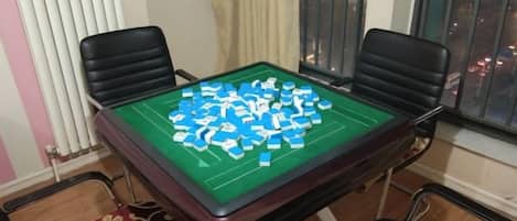 Una habitación con una mesa verde para un juego de mesa, cuatro sillas, una ventana con persianas y un radiador.