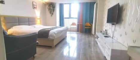 Una habitación de hotel con cama, escritorio, televisor y ventana con cortinas.