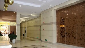 A modern hotel lobby with a marble floor, a reception desk, and a decorative wall with a floral pattern. - Zhengzhou Wanda Hotel (Erqi Wanda) (Zhengzhou)