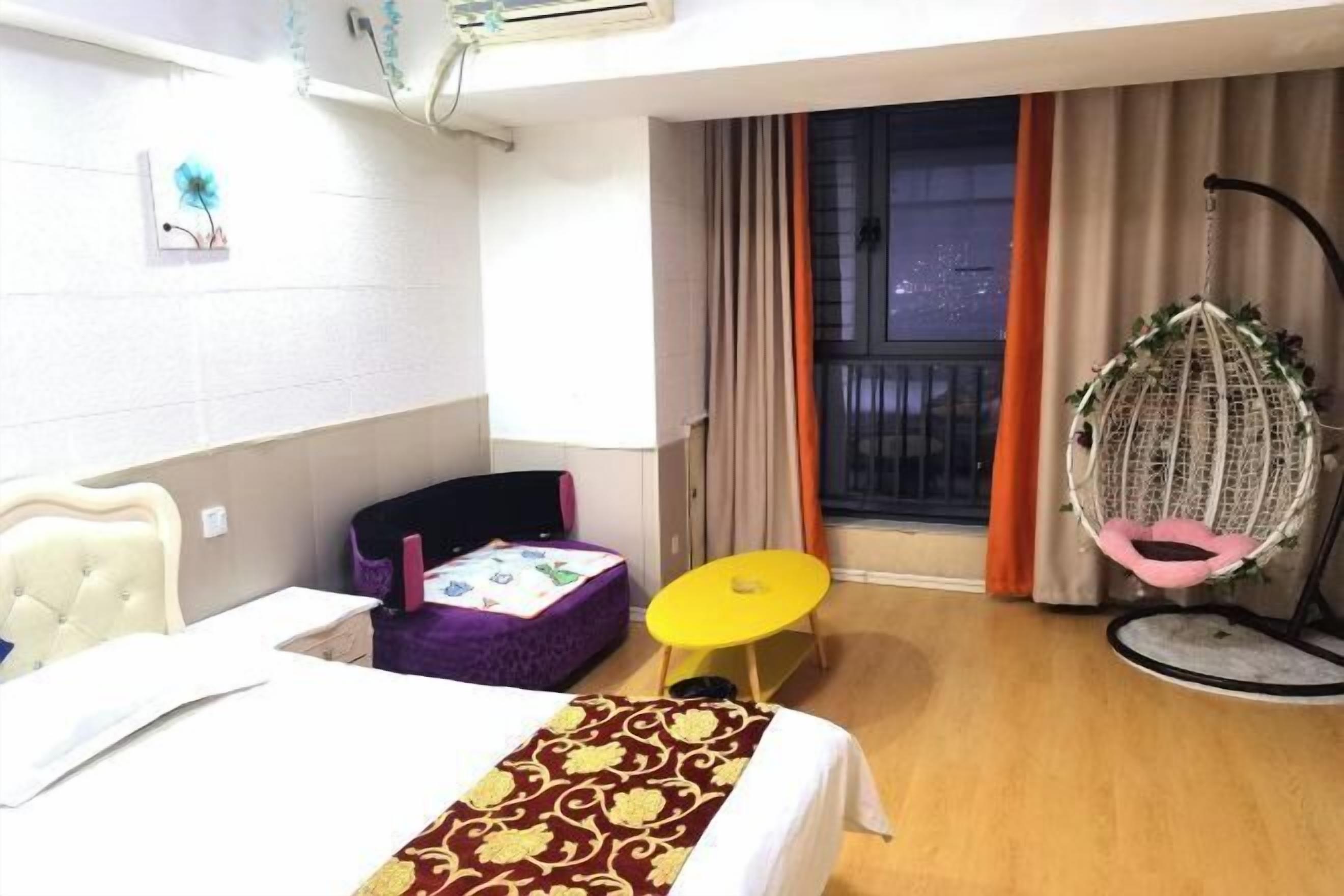 Una camera d'albergo con un letto, un piccolo tavolo, una sedia, una poltrona sospesa e una finestra con tende.
