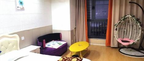 Una camera d'albergo con un letto, un piccolo tavolo, una sedia, una poltrona sospesa e una finestra con tende.