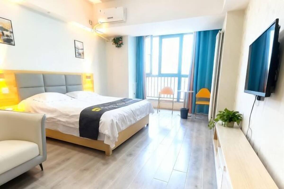 Una habitación de hotel con cama, una silla, televisor, balcón y planta en maceta.