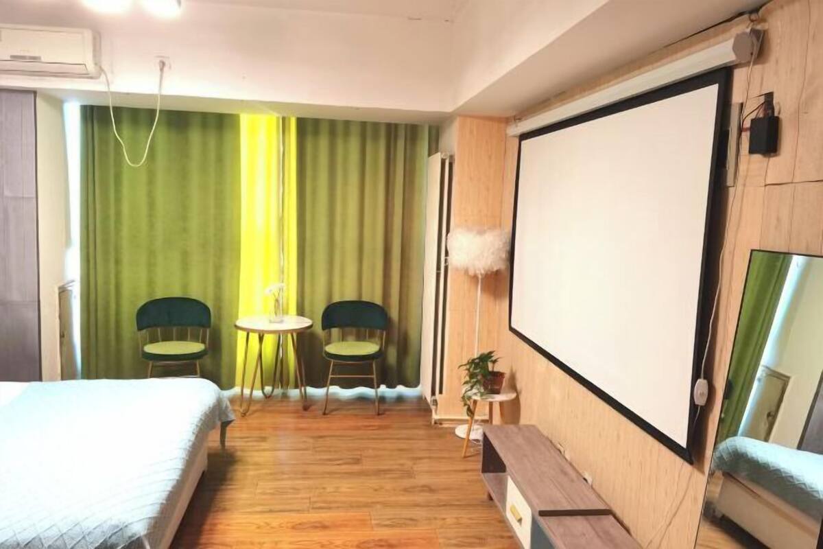 Habitación de hotel con cama, escritorio, dos sillas, una mesita, espejo y un amplio ventanal con cortinas.