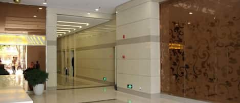 A spacious lobby with a reflective floor, a potted plant, and a decorative wall with intricate patterns.