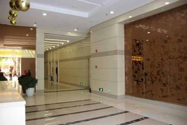 A spacious lobby with a reflective floor, a potted plant, and a decorative wall with intricate patterns.