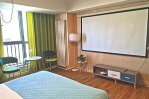 Une chambre d’hôtel équipée d’un lit, d’un bureau, de deux chaises, d’une petite table, d’un écran de projection et d’un radiateur.
