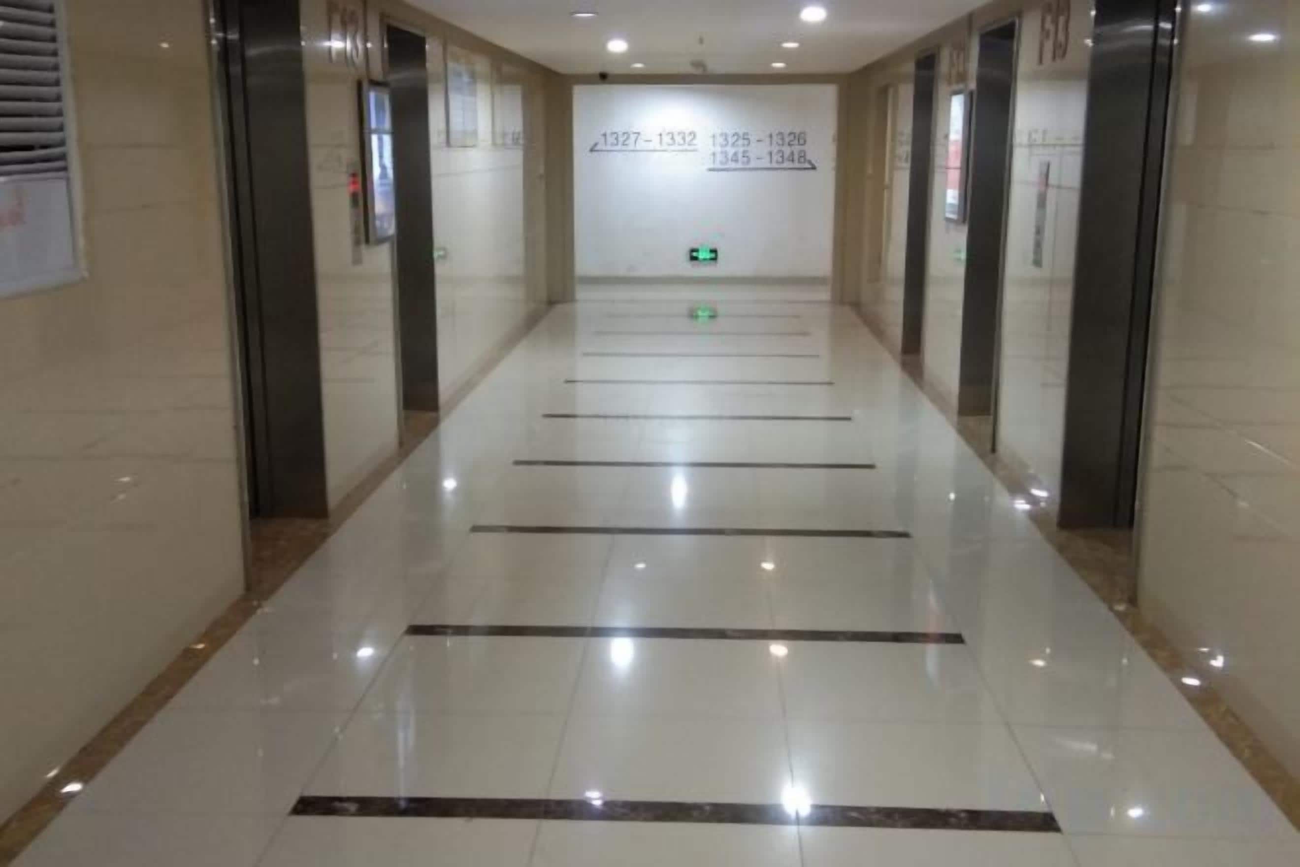 Un pasillo con piso pulido, señales de salida de emergencia y puertas de ascensor.