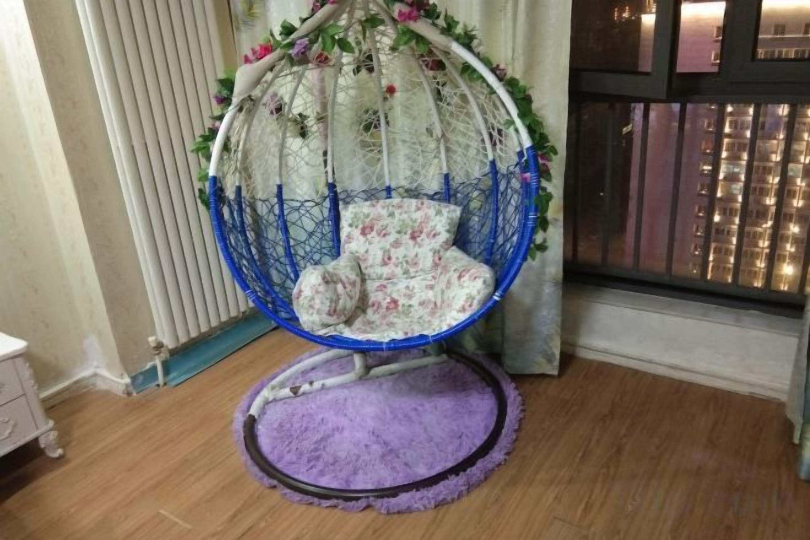 Una silla colgante con un cojín estampado con motivos florales en una habitación con suelo de madera y una alfombra morada.
