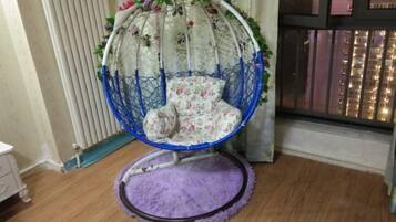 Una silla colgante con un cojín estampado con motivos florales en una habitación con suelo de madera y una alfombra morada.