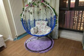 Una cadira penjant amb un coixí floral en una habitació amb terra de fusta i una catifa morada.