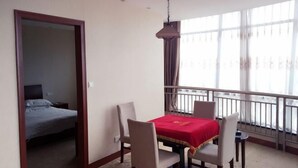 Una habitación de hotel con balcón, una mesa de comedor con mantel rojo y una cama con cabecera gris.