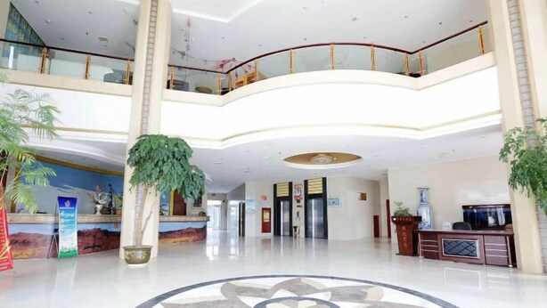 Un vestíbulo amplio con un piso circular de mosaicos en el centro, un mostrador de recepción y una escalera que conduce a un nivel superior.