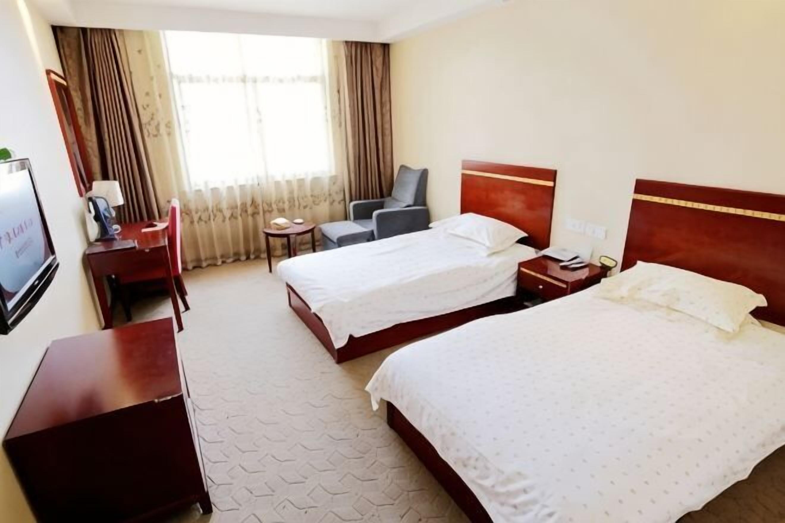 A hotel room with two beds, a desk, a chair, a TV, and a window with curtains.