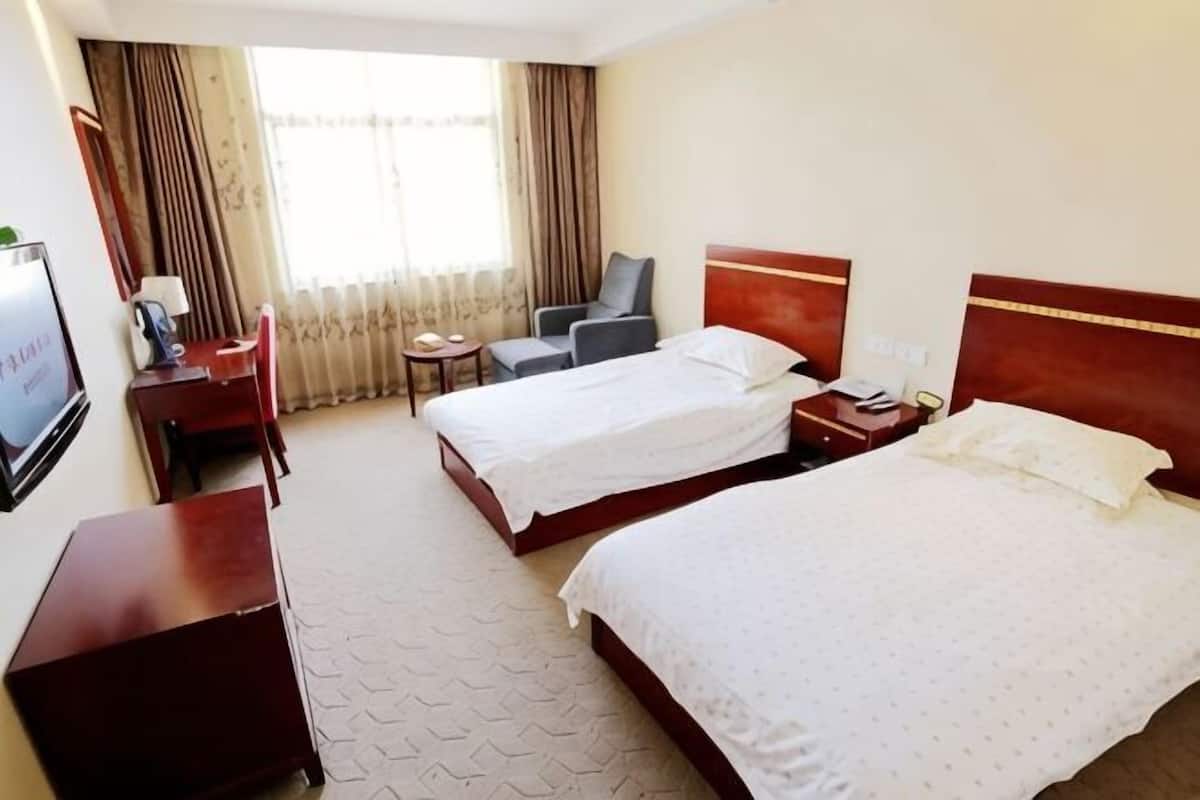 A hotel room with two beds, a desk, a chair, a TV, and a window with curtains.
