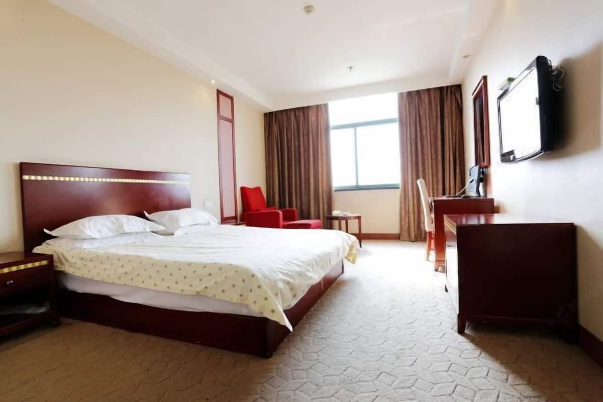 A hotel room with a large bed, a desk, a chair, a TV, and a window with curtains.