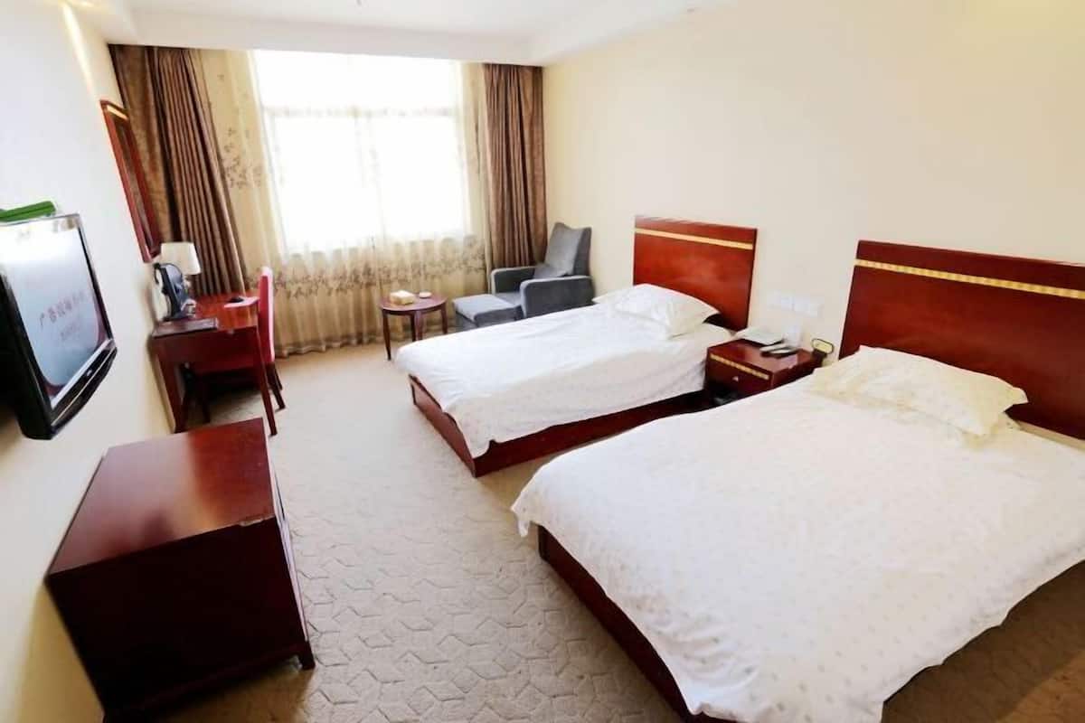 A hotel room with two beds, a desk, a chair, a TV, and a window with curtains.