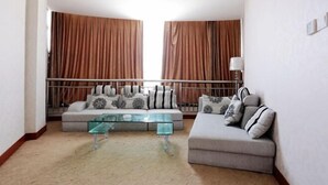 Un salón con dos sofás, una mesa de centro de vidrio y vistas a través de cortinas grandes.