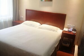 A hotel room with a large bed, a wooden headboard, a nightstand with a lamp, and a small trash bin. - Wanhao Hotel (Cixi)