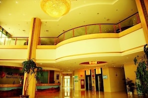 A multi-level hotel lobby with a grand chandelier, a curved ceiling, and a glass railing on the upper level.