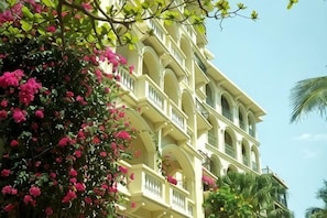 A multi-story building with balconies, surrounded by lush greenery and flowering plants.