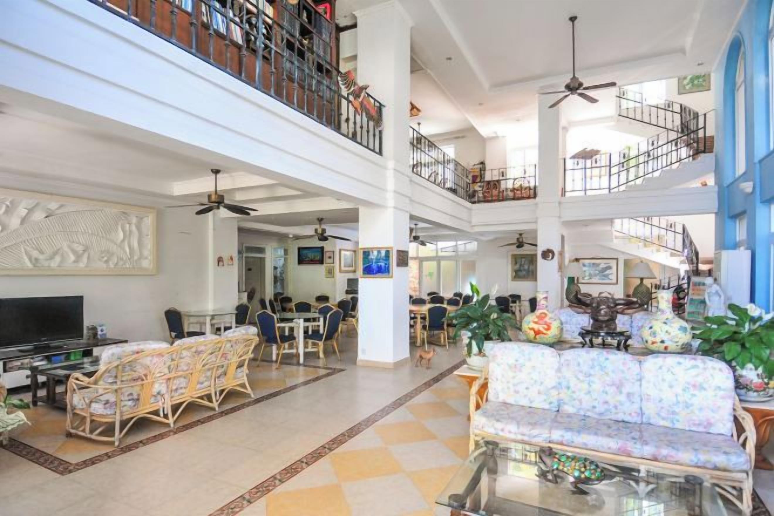 A spacious hotel lobby with multiple seating areas, a central television, and a staircase connecting the floors.