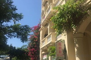 Hotel amb balcons, una placa senyalitzadora i vegetació exuberant.