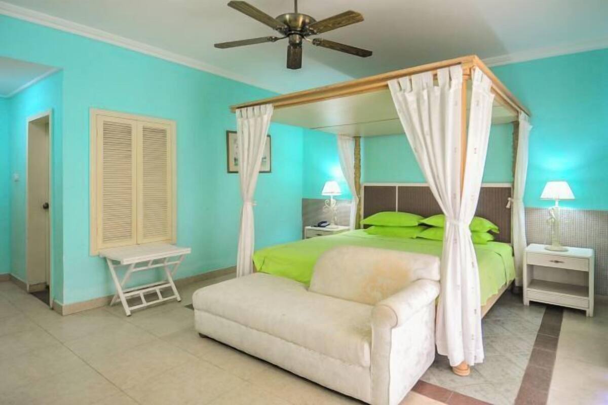 Une chambre à coucher avec un lit à baldaquin, un canapé, une table de chevet, un bureau et un ventilateur de plafond.