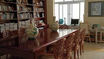 Un comedor con una mesa de madera larga, sillas, una estantería con libros y jarrones decorativos.