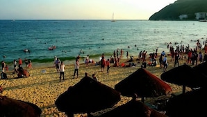 Una playa con gente, un velero y una colina al fondo.