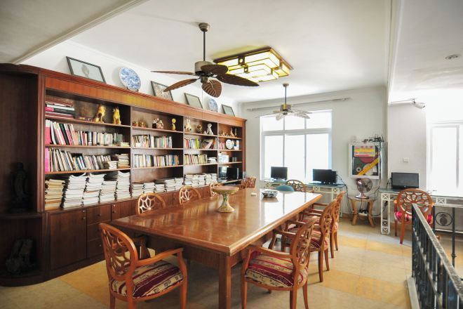 A spacious dining area with a long wooden table surrounded by chairs, a large bookshelf filled with books, and a ceiling fan.