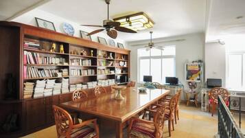 A spacious dining area with a long wooden table surrounded by chairs, a large bookshelf filled with books, and a ceiling fan.